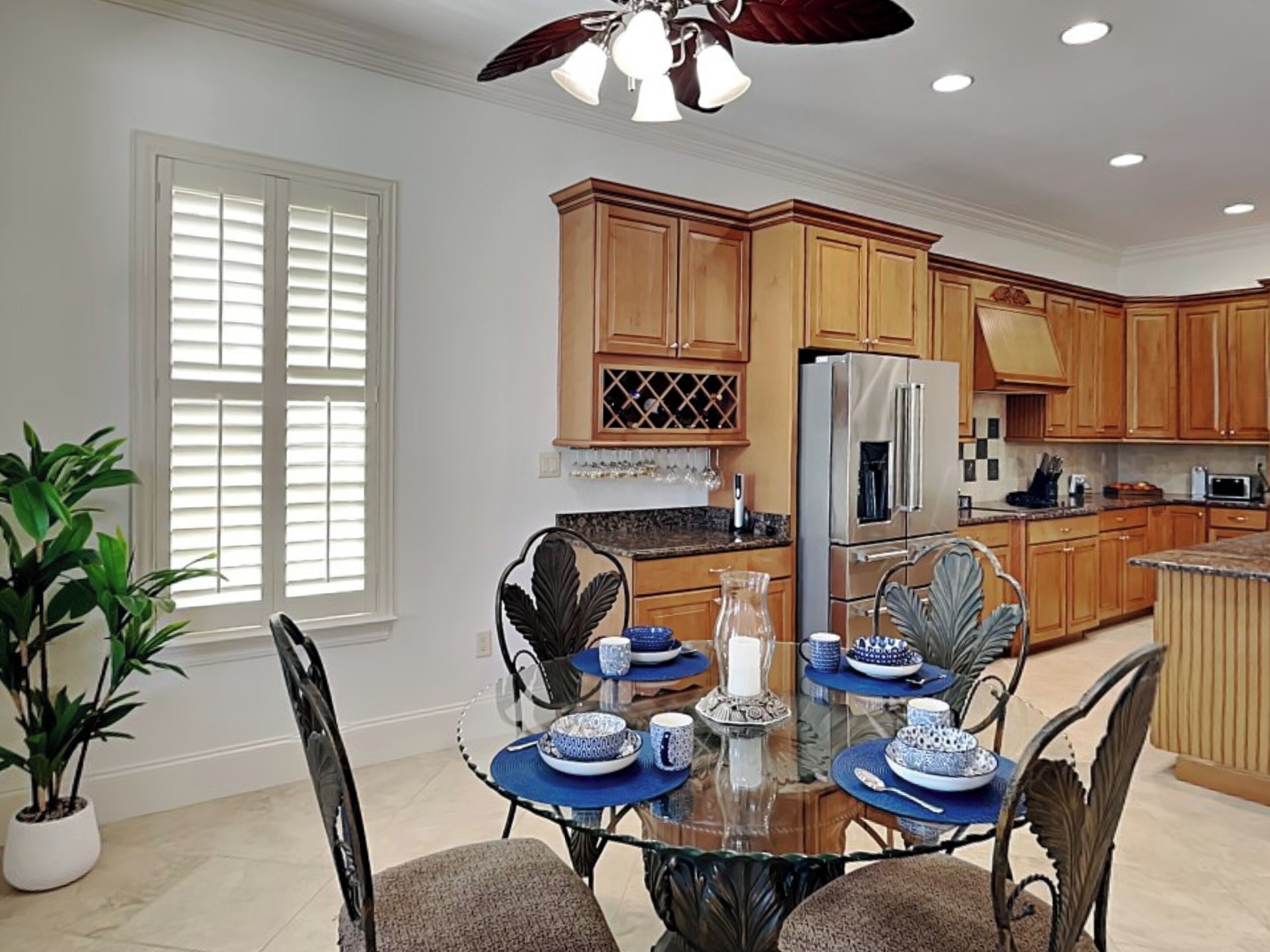A modern kitchen with wooden cabinets, stainless steel appliances, and a dining area with a glass table and blue placemats.