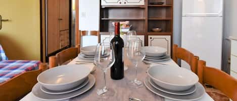 A dining table set with plates, wine glasses, and cutlery, with a bottle of wine and a corkscrew on the table.