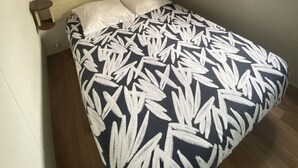 Un dormitorio con una cama, un televisor montado en la pared, una ventana con cortinas y un estante pequeño sobre la cama.