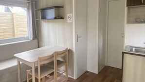 Una cocina pequeña y bien iluminada con una mesa y sillas de madera, una ventana con cortinas, un reloj y un cartel de prohibido fumar.