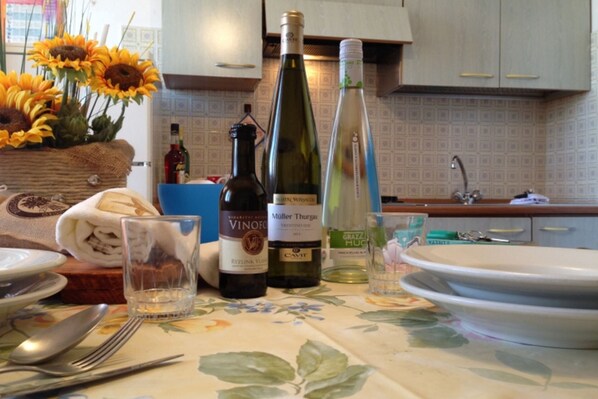 A kitchen with a floral tablecloth, a bottle of Müller Thurgau wine, a bottle of white wine, and a vase of sunflowers. - Nice Apartment Close to the sea (Rosolina)