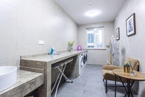 A compact hotel bathroom with a sink, washing machine, and a small table with a chair. - Homeinn Plus Hotel (Qingdao Weihai Road Taidong Pedestrian Street) (Qingdao)
