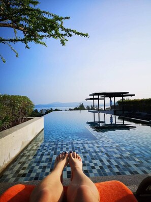 A poolside view with a clear sky, a tiled pool, and a structure with a roof.