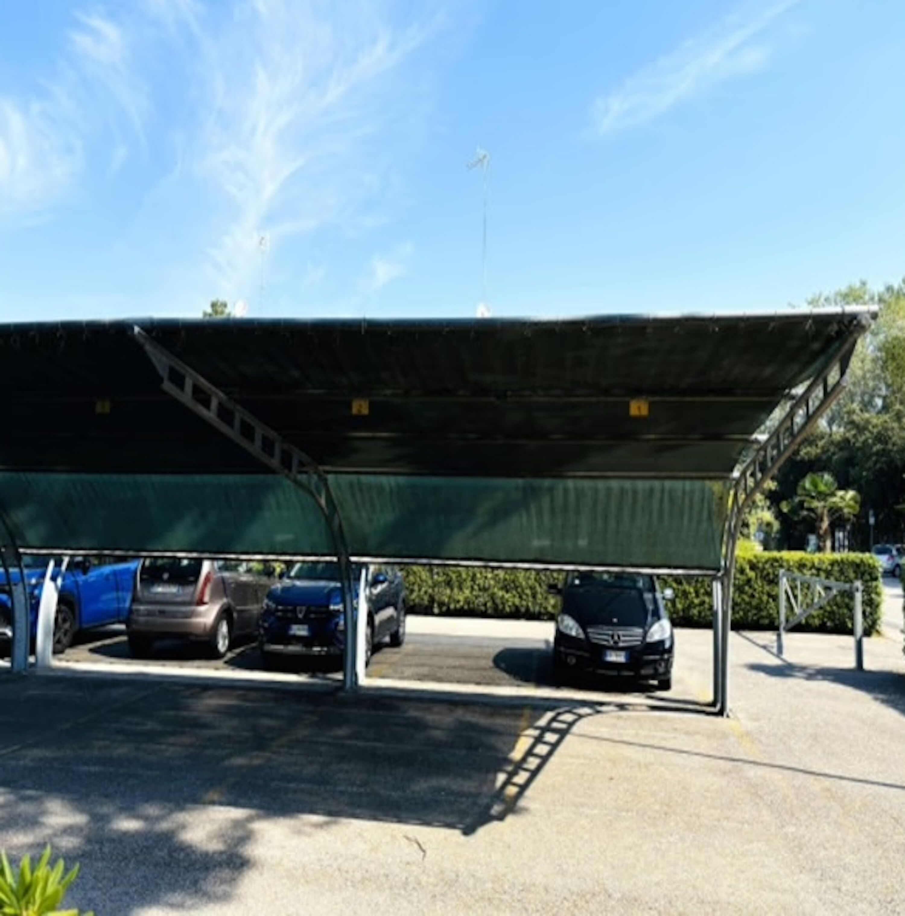A covered parking area with multiple cars parked under a green canopy.