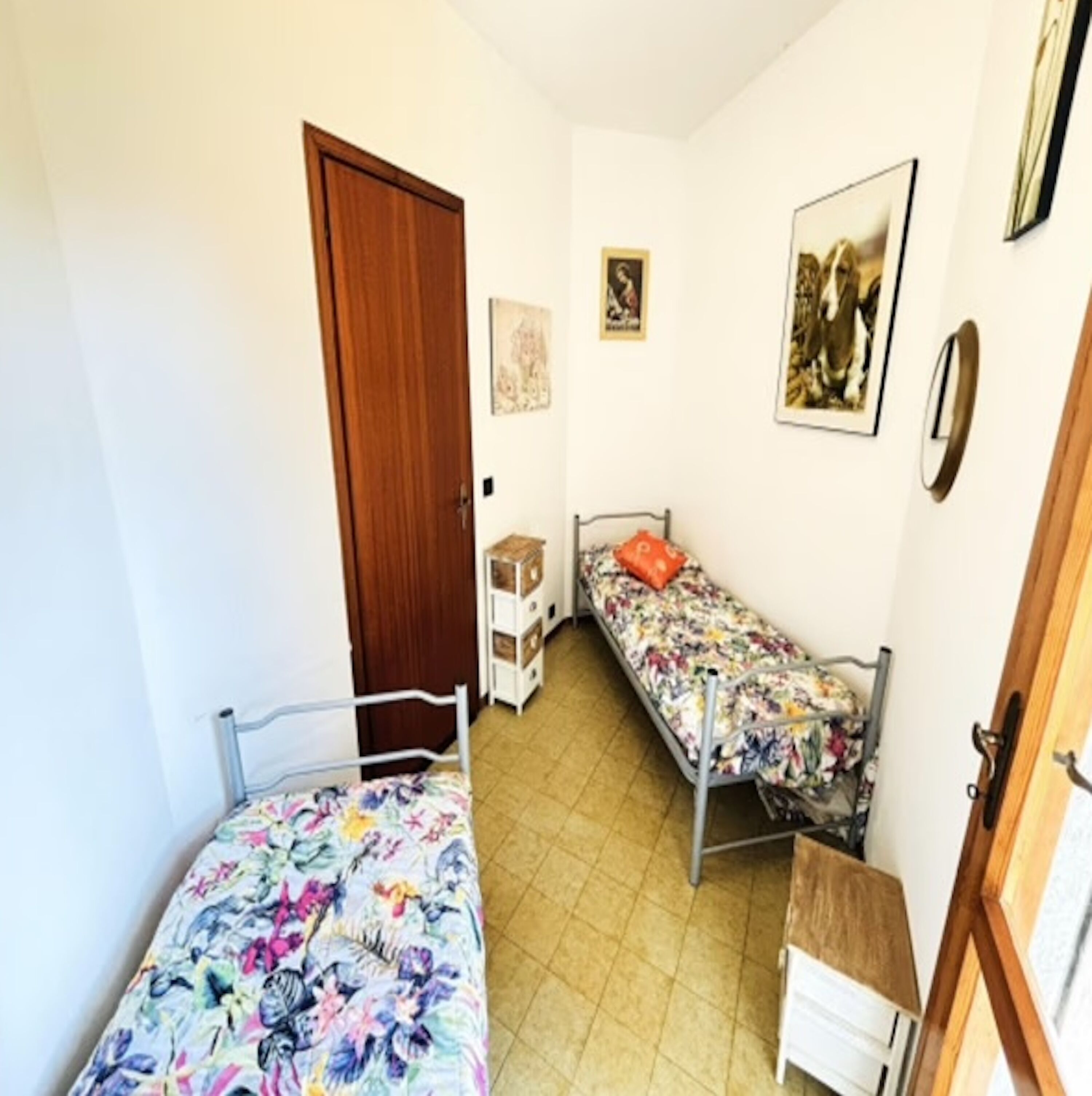 A small, narrow room with two single beds, a wooden door, and a small cabinet.