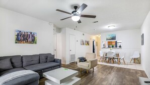 A modern living room with a grey sofa, a white coffee table, and a beige armchair. There is a dining area with white chairs and a kitchen visible in the background. - Baton Rouge-Pet friendly, 2BR/2BA, Near LSU (Baton Rouge)