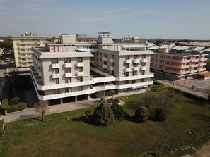 A multi-story residential building with balconies, a parking area, and a small park with trees. - Seafront Studio With Balcony (San Michele al Tagliamento)