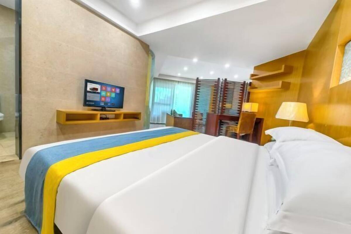 A hotel room with a bed, a television, a desk, and a window.
