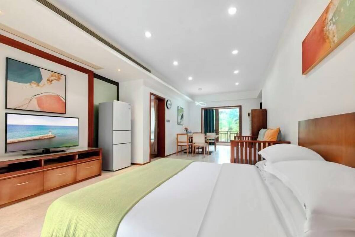A hotel room with a bed, a television, a desk, and a balcony with a view of the outdoors.