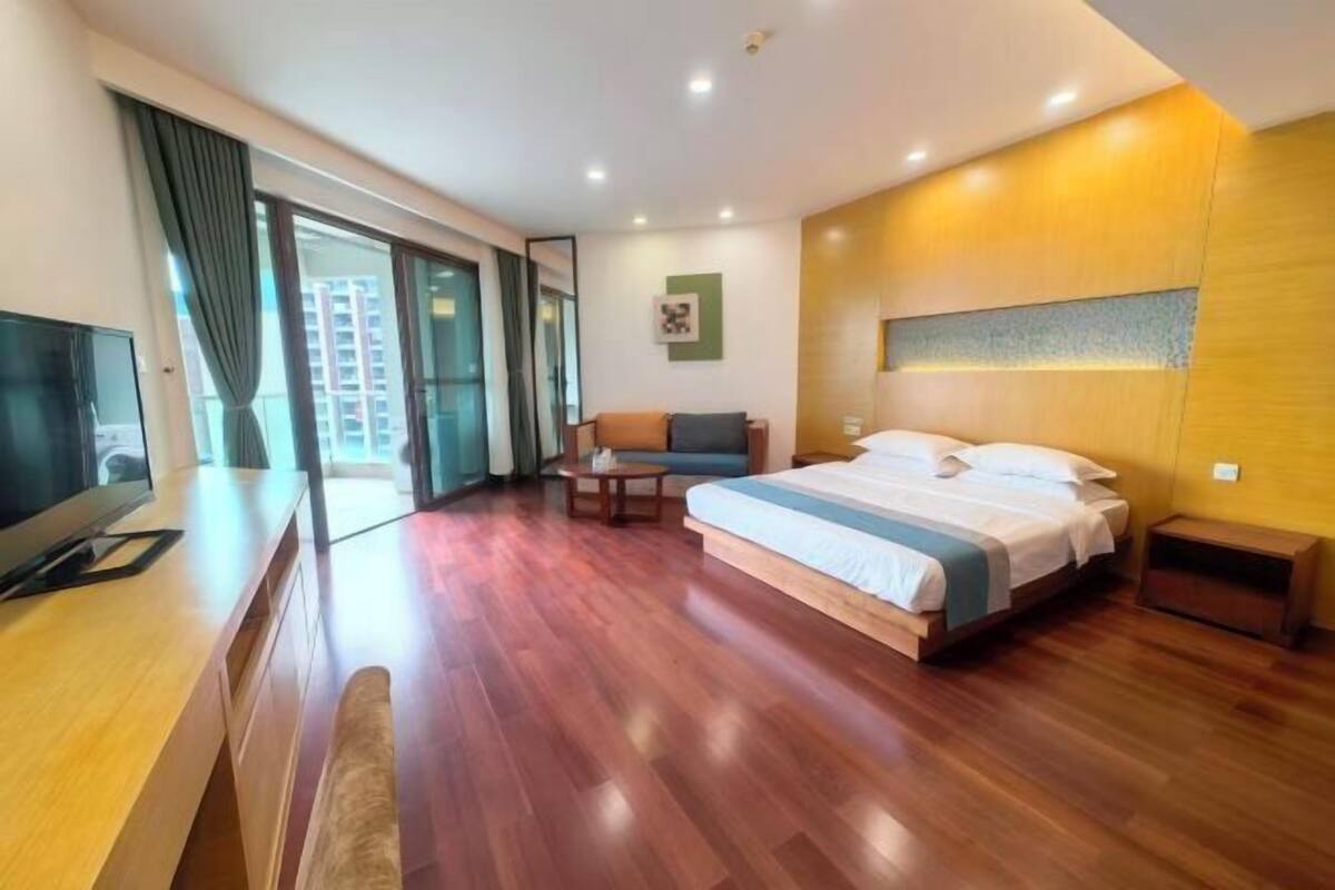 A modern hotel room with a large bed, a desk, a sofa, and a TV.