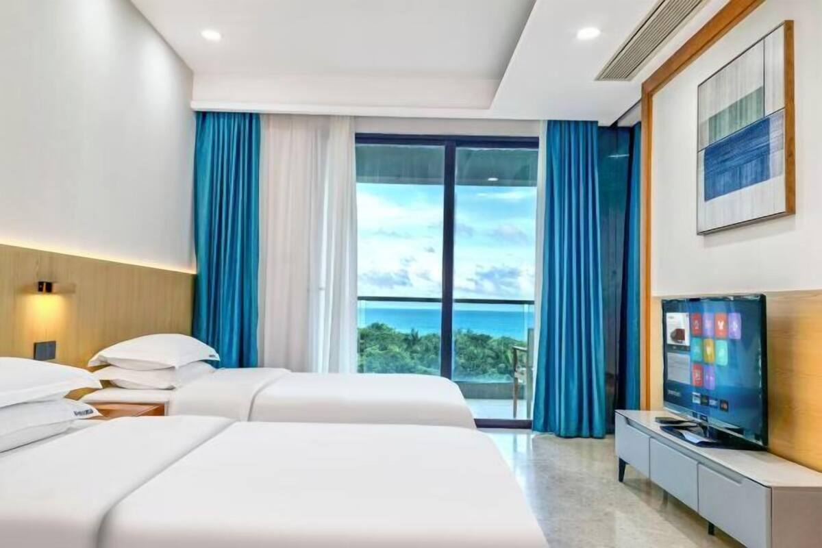 A hotel room with two beds, a TV, and a large window with a view.