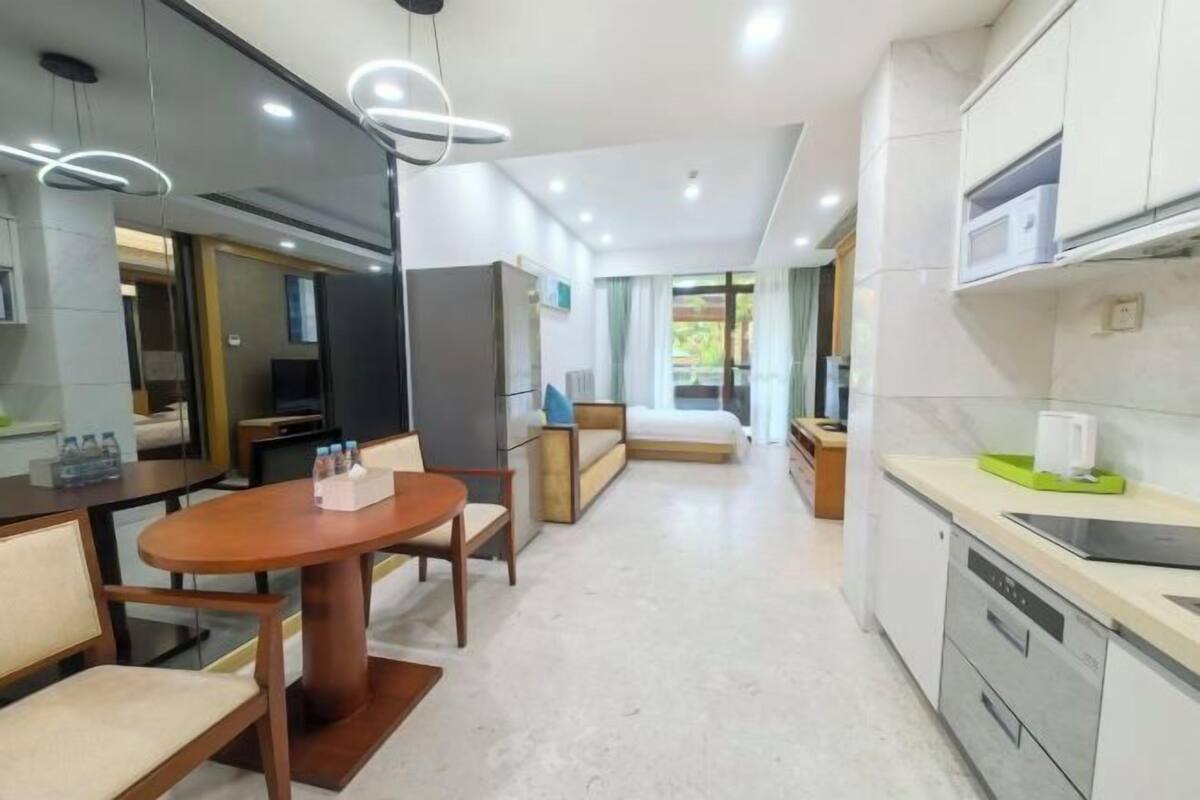 A modern hotel room with a dining area, kitchenette, and a seating area with a sofa and chairs.