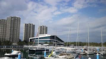 A marina with multiple boats docked, a modern building with a curved facade, and tall residential buildings in the background.