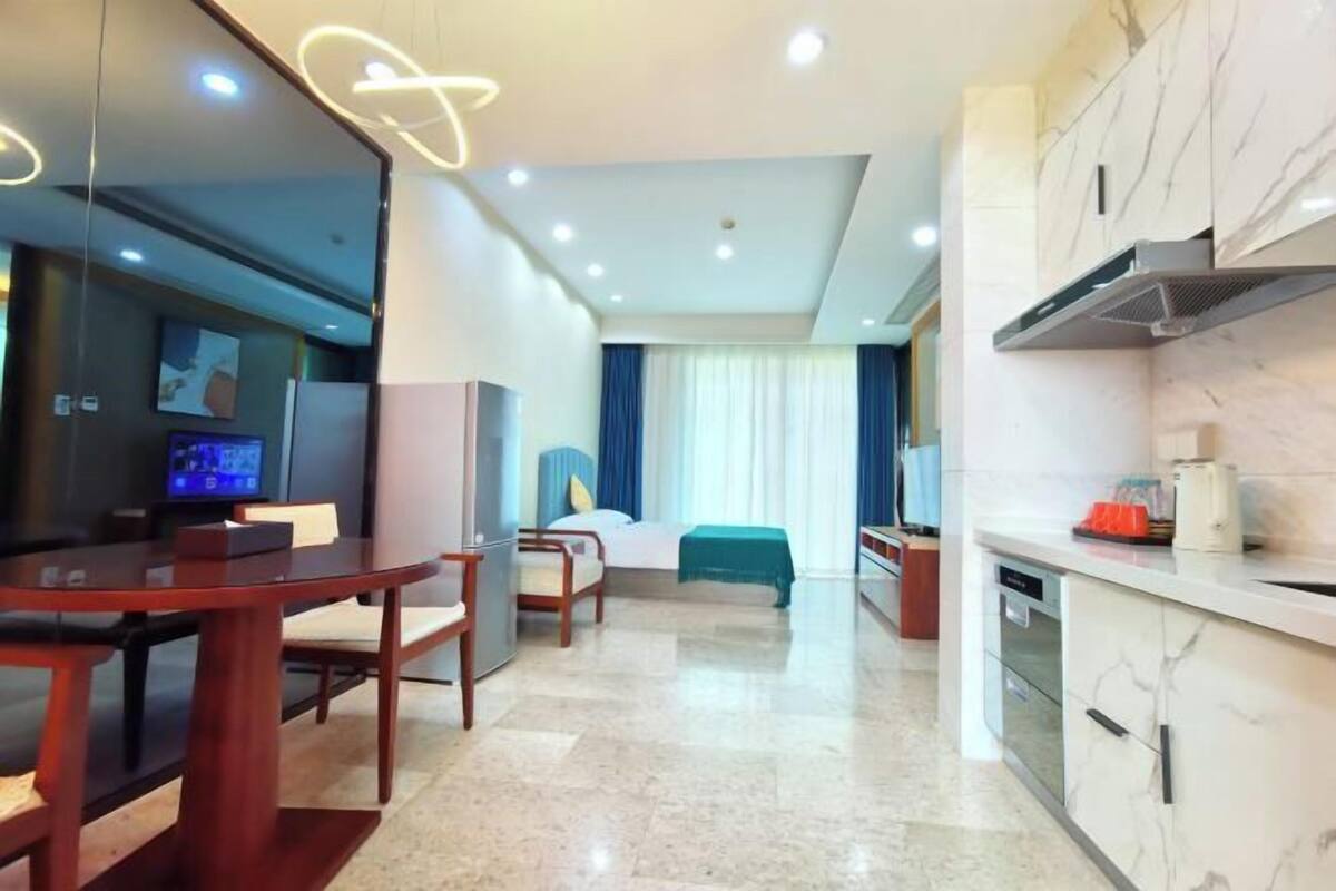 A modern hotel room with a dining area, a bed, a TV, and a kitchen.