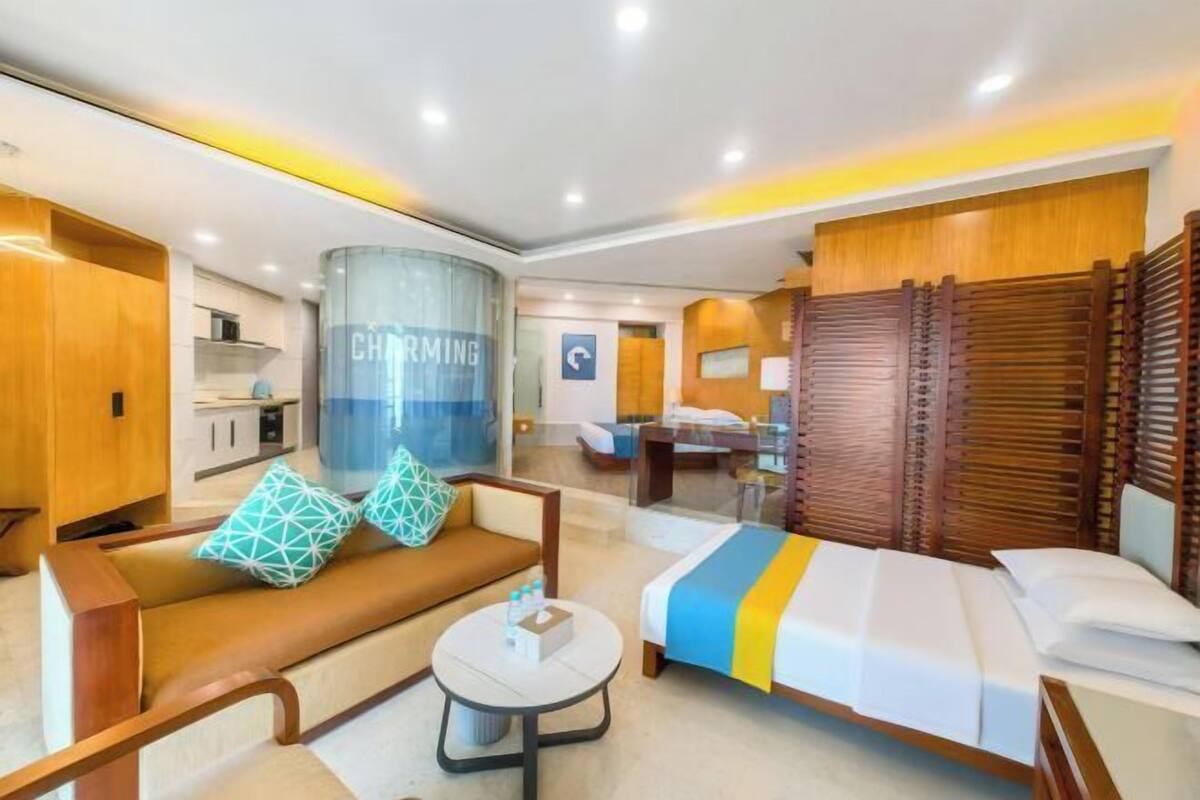 A hotel room with a sofa, a bed, a round table, and a kitchenette area.