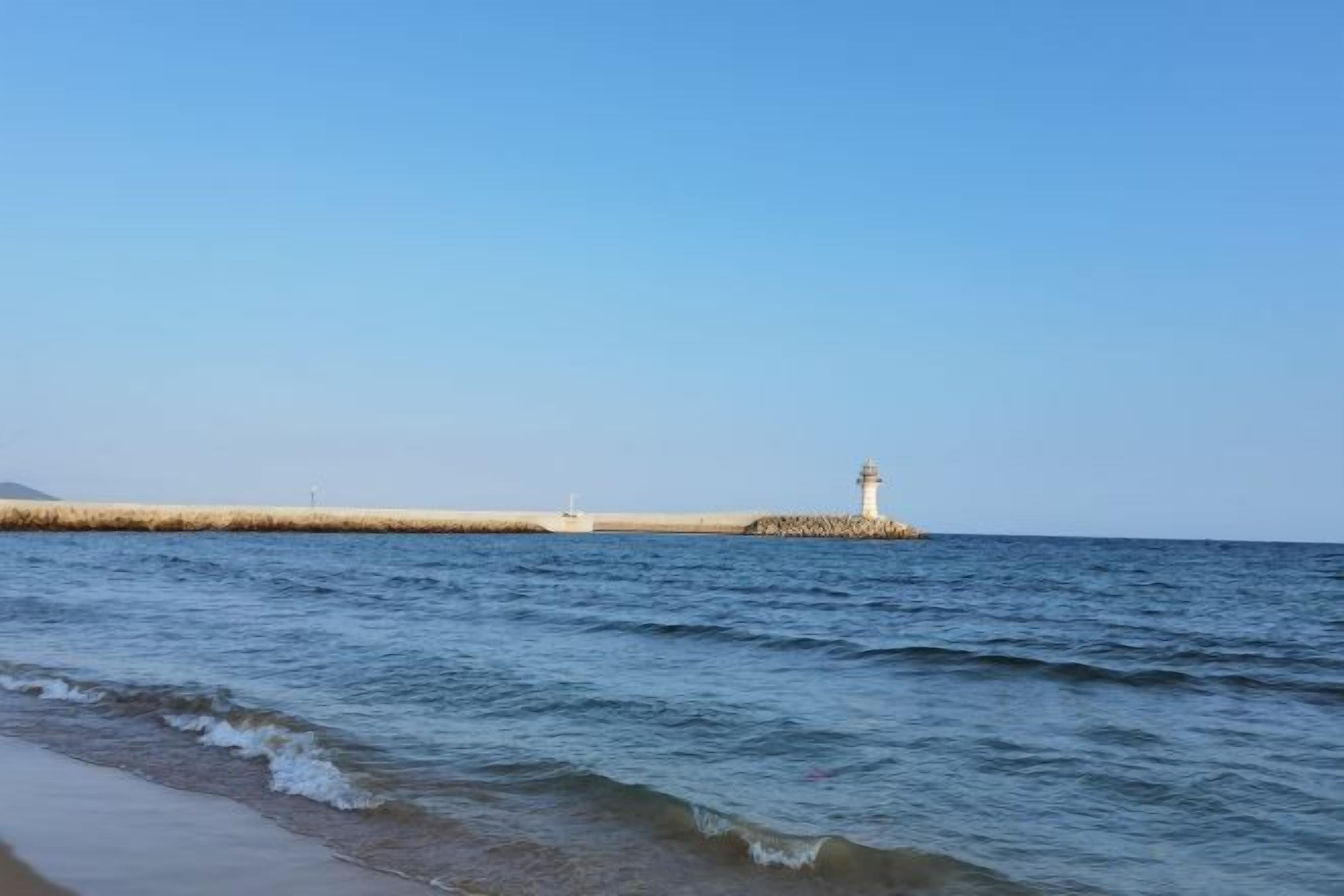 Escena costera con aguas tranquilas, un faro y una costa distante.