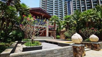 A hotel courtyard with a modern building, palm trees, and a well-maintained garden.