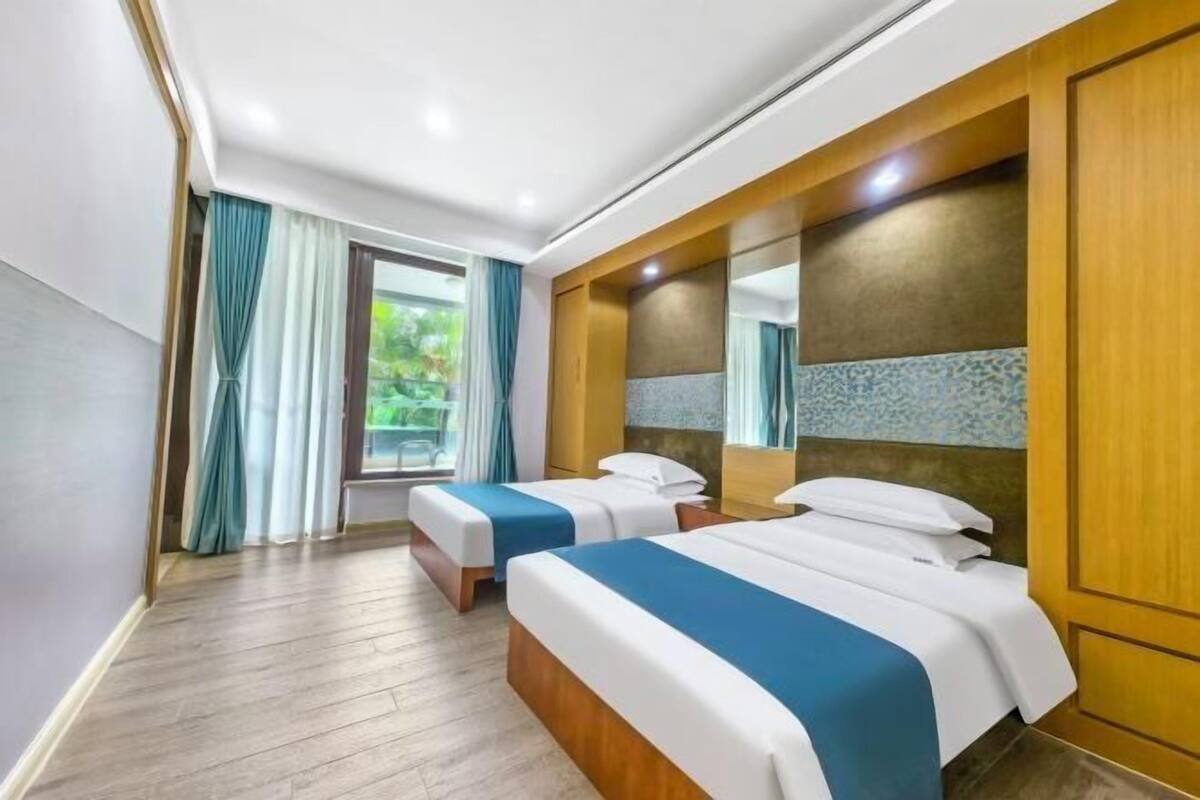 A hotel room with two beds, a large window with curtains, and a wooden headboard.