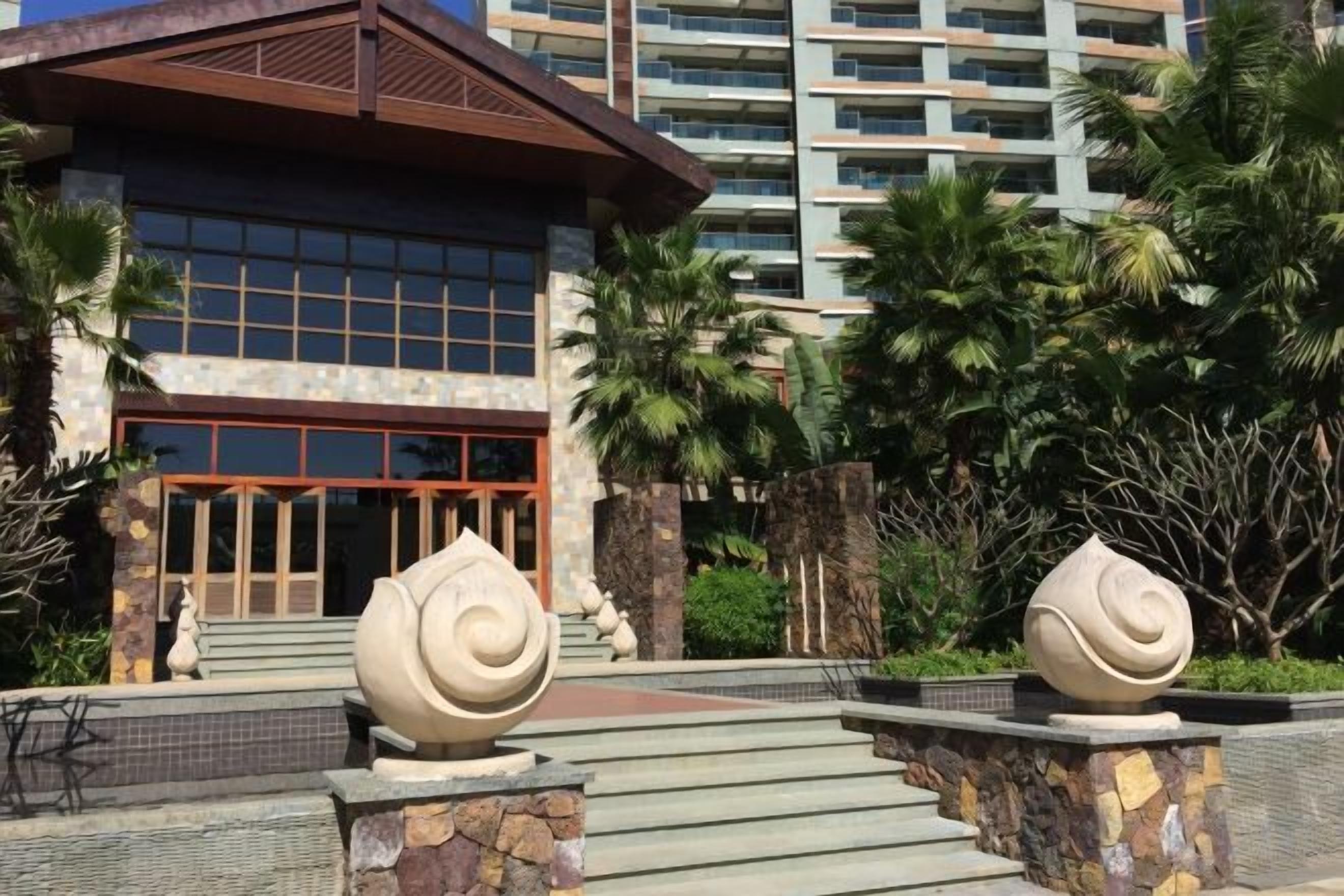 A hotel entrance with a modern facade, a stone staircase, and palm trees in the background.
