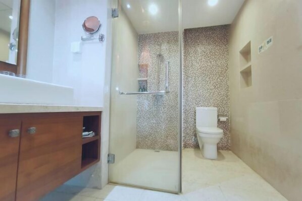 A bathroom with a shower, toilet, and wooden vanity. - Ocean Holiday Apartment (Lingshui)