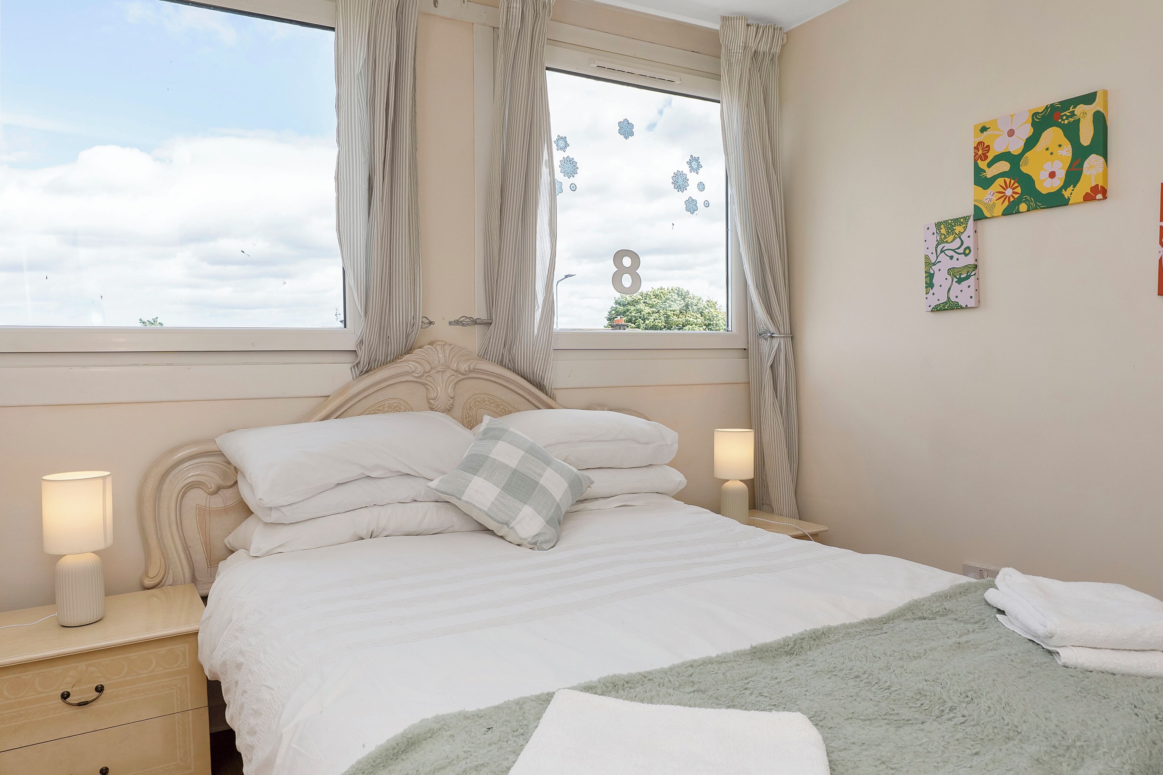 A bedroom with a bed, nightstands, a window with curtains, and wall art.