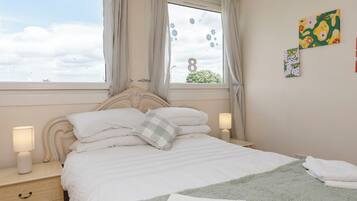 A bedroom with a bed, nightstands, a window with curtains, and wall art.