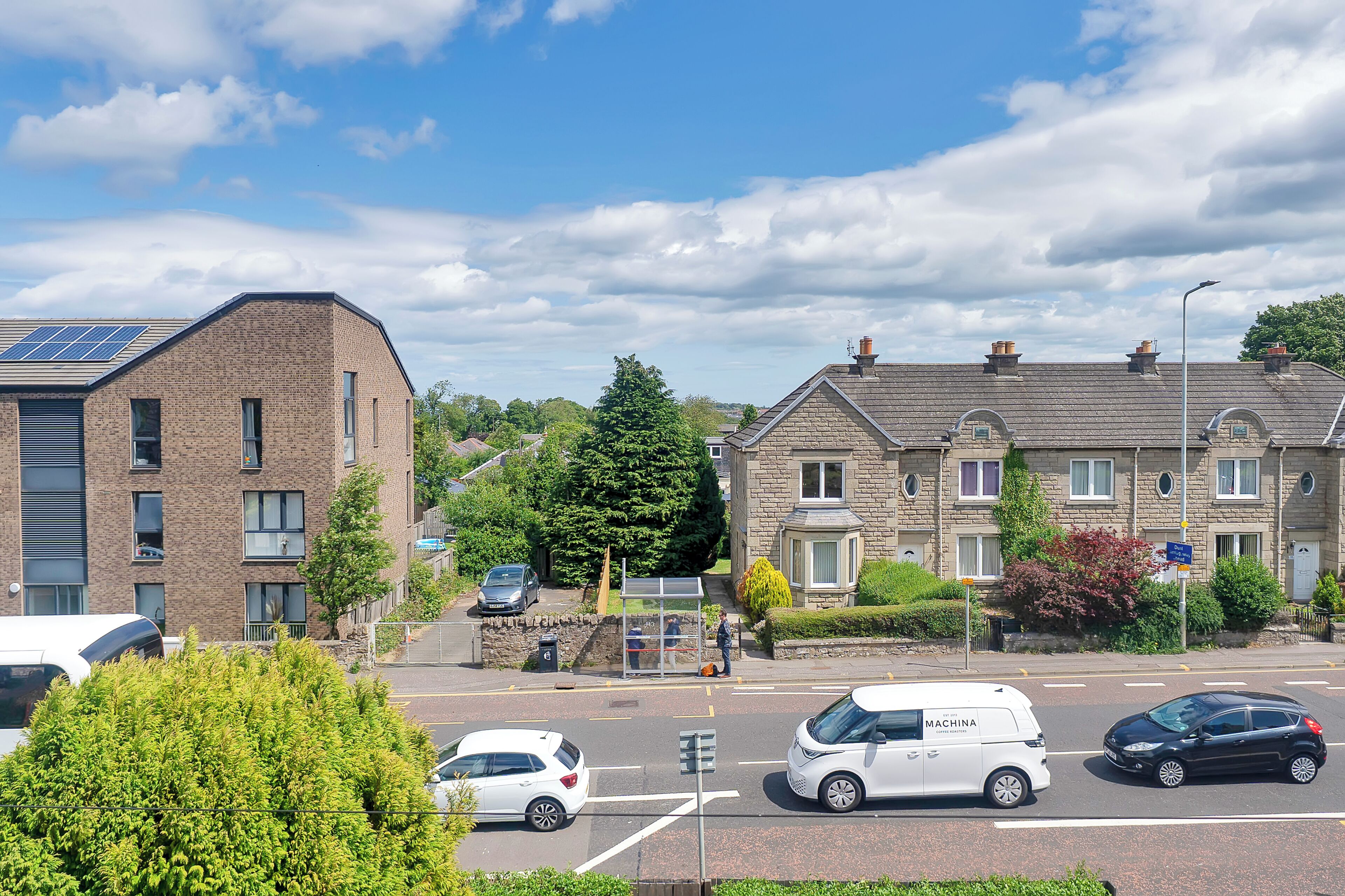 A residential street with houses, a bus stop, and parked cars.