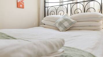 A neatly made bed with white bedding and a checkered pillow, a metal headboard, and a wall with a framed picture.