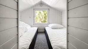 Una pequeña cabaña individual con dos camas, una ventana y techo inclinado.