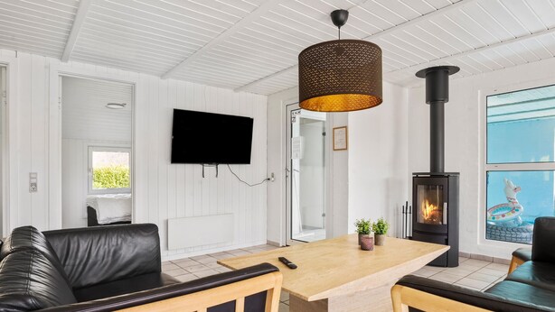 Una sala de estar moderna con un sofá de cuero negro, una mesa de centro de madera, un televisor montado en la pared, un estufa de leña negra y una puerta de vidrio que da a un balcón.