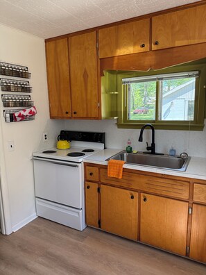 A kitchen with wooden cabinets, a white stove, a stainless steel sink, and a window with a view of the outside.