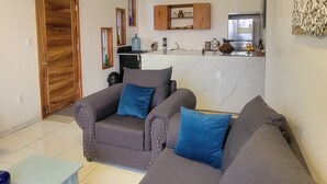 Una sala de estar con un juego de sofá, una mesita de centro y una cocina al fondo.