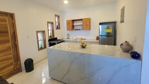 Una cocina moderna con encimera de mármol, armarios de madera, estufa integrada y refrigerador.