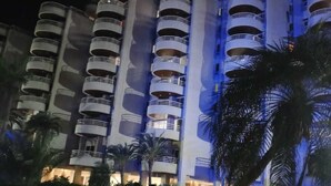 Een meerlaags hotel met balkons, een zwembad en palmbomen.