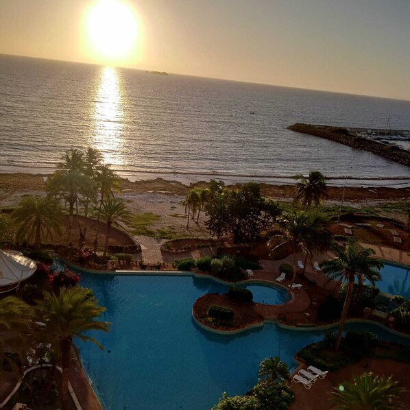 A resort pool with a view of the ocean and beach at sunset. - Venetur Margarita (Mariño)