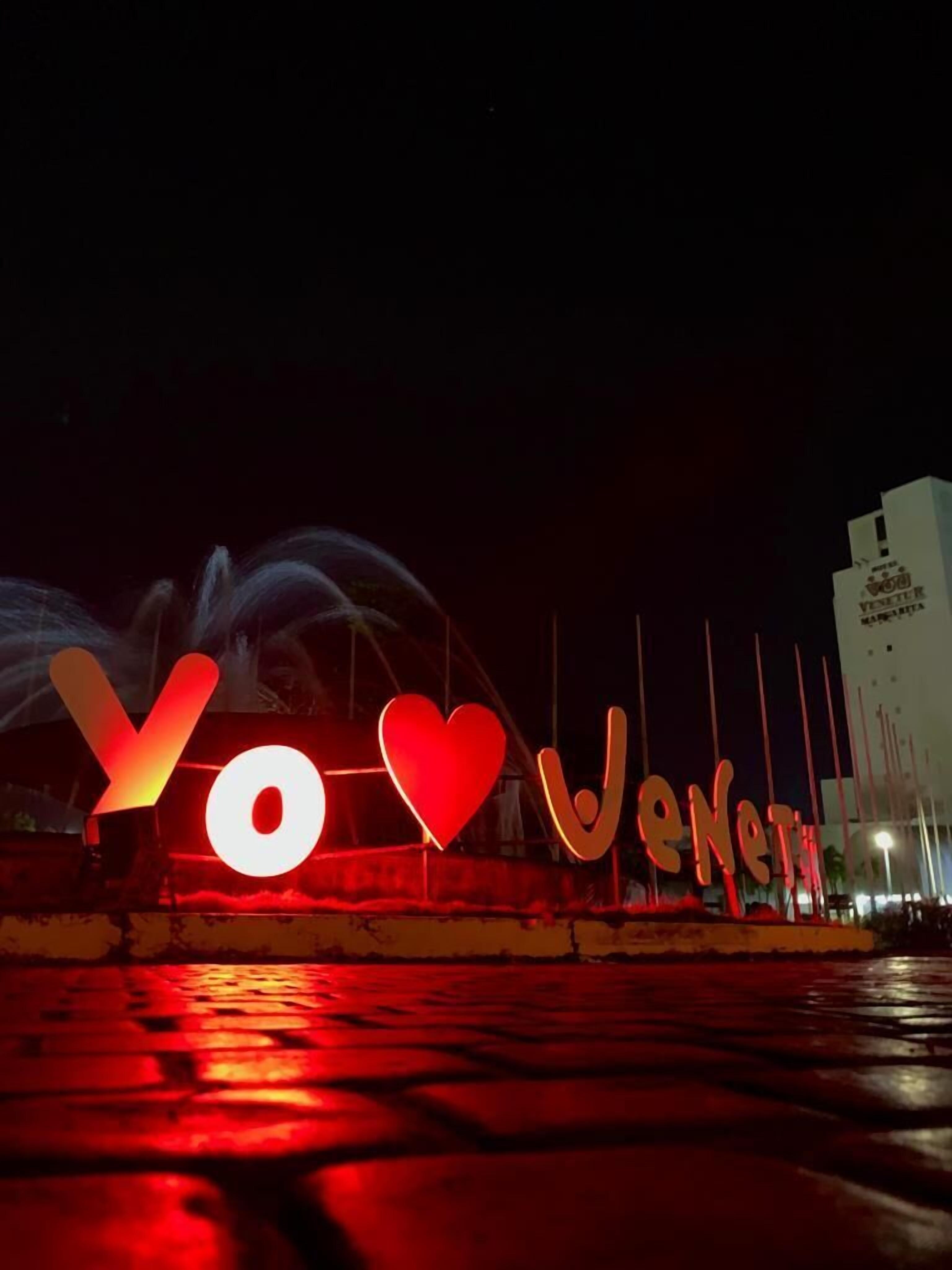 Illuminated letters spelling "YO VENEZUELA" on a wet surface at night.