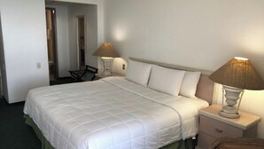 Een keurig opgemaakt bed met witte lakens, een bedlampje en een stoel in een hotelkamer.