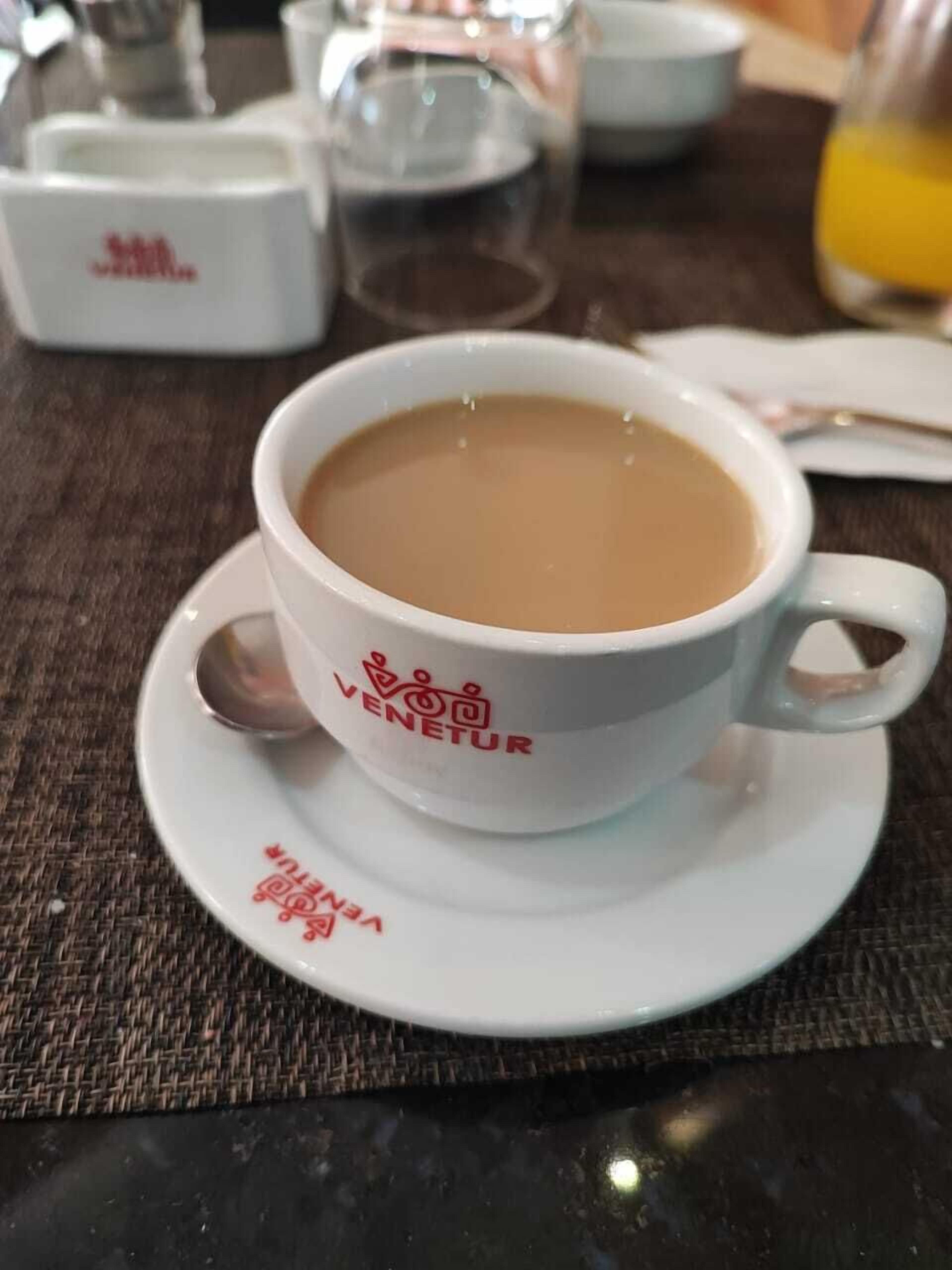Une tasse de café posée sur une soucoupe ornée du logo « VENETUR », le tout placé sur une table recouverte d’un set de table en fibres tressées.