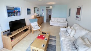 A modern living room with a flat-screen TV, wooden furniture, a sofa, and a dining table.