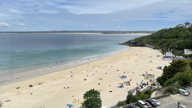 A beach with a sandy shore, a few people, and a building on a hill.
