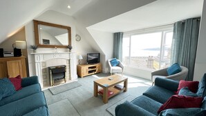 A modern living room with a fireplace, a television, and a view of the sea.