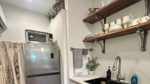 Een keuken met een koelkast, een spoelbak, houten planken en een raam met gordijnen.