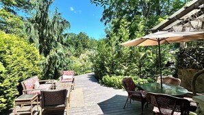 Een buitenterras met houten terras, rieten meubels en een pergola voor beschutting.