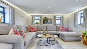 A spacious living room with a grey sectional sofa, a round coffee table, and a large window with curtains. - The Gate House (Richmond)