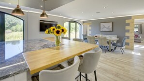 A modern kitchen with a wooden island, a large window, and a dining area with a table and chairs. - The Gate House (Richmond)