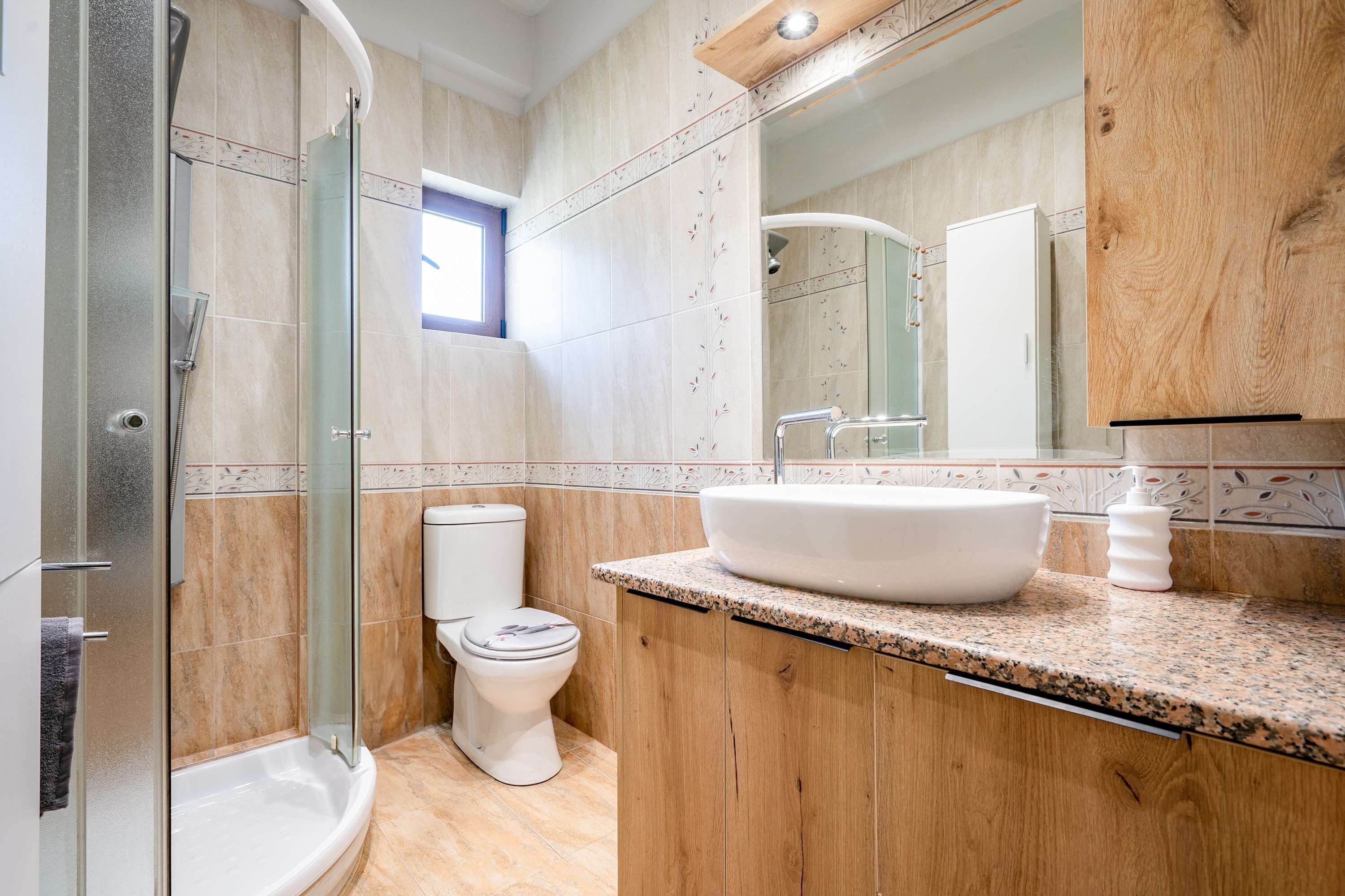 Ein Badezimmer mit einer Duschkabine aus Glas, einer Toilette, einem Waschbecken mit großzügiger Schale und Holzschränken.