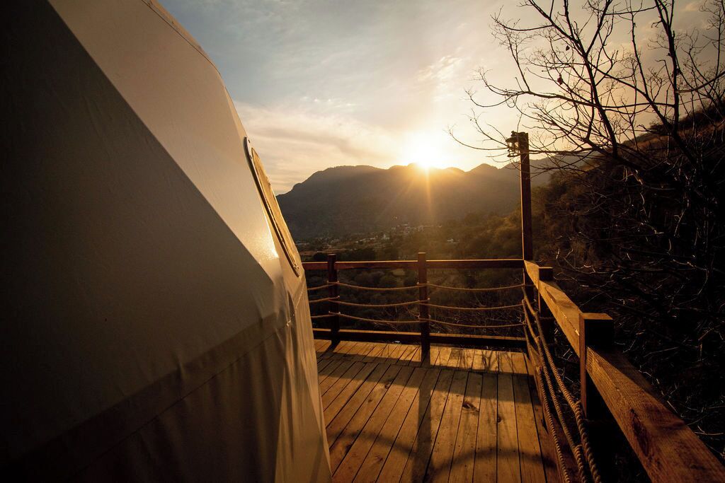 Eine Holzterrasse mit Seilgeländer, mit Blick auf eine Berglandschaft im Abendlicht.