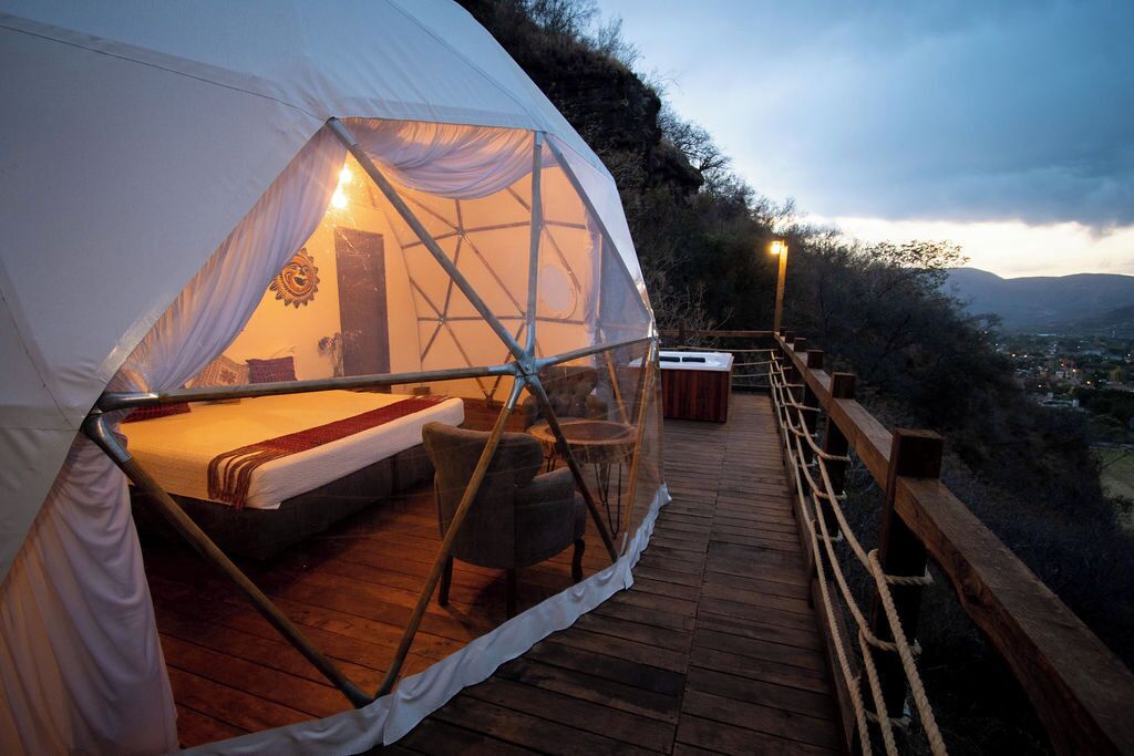 A tent with a bed and seating area, a wooden deck, and a view of the landscape.