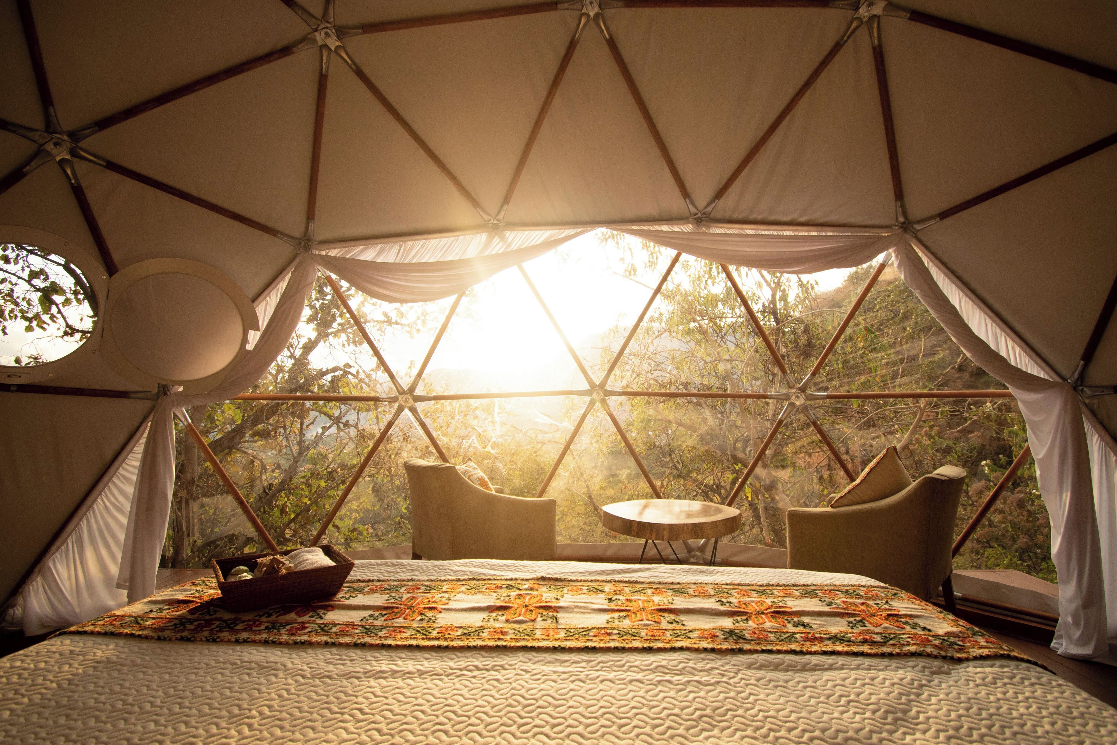 Un hébergement sous tente comprenant un lit, une petite table et des chaises, le tout situé dans un cadre naturel.