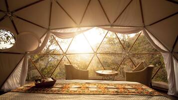 Un hébergement sous tente comprenant un lit, une petite table et des chaises, le tout situé dans un cadre naturel.